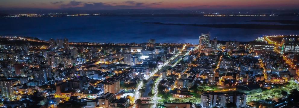 vista aérea ao anoitecer da cidade, com Guaíba ao fundo.